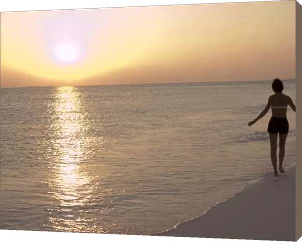 Girl walking on the beach at sunset in the Maldives