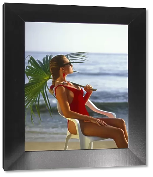 Kirsten Imrie in red swim suit, seated holding palm leaf