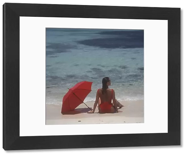 Girl sitting on the beach with red umbrella