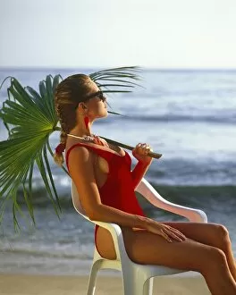 Travel Collection: Kirsten Imrie in red swim suit, seated holding palm leaf